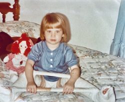 Cindy, age 3 sitting on bed with leg casts on with 2 bars to keep legs separated
